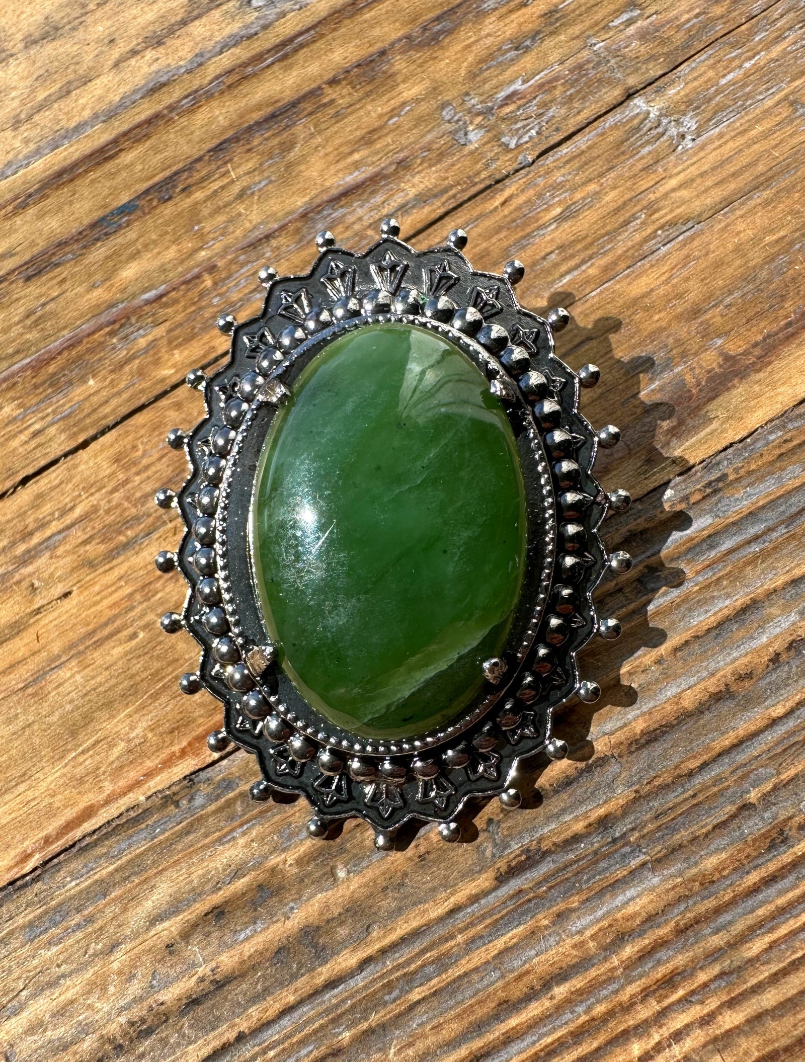 Vintage jade oval brooch with a green central stone framed by ornate silver filigree and a beaded border.