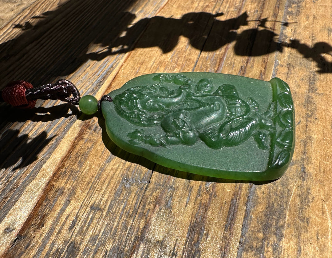 Green jade Ganesha Buddha pendant with detailed carving resting on a wooden surface.