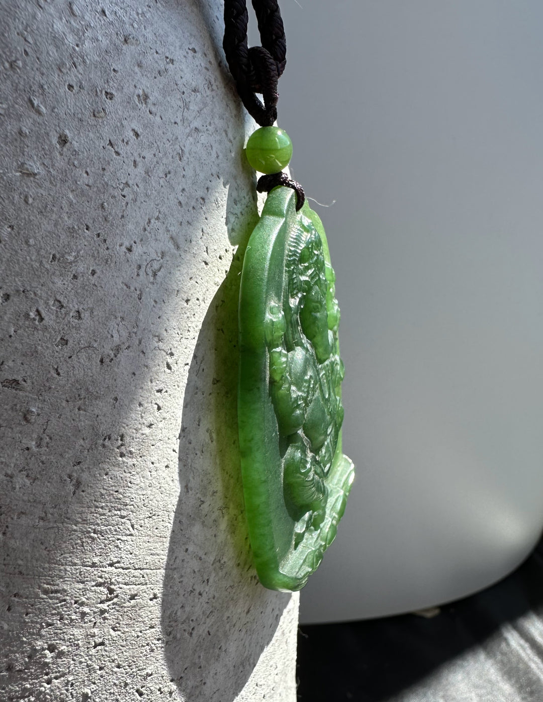 Side view of green jade Ganesha Buddha pendant on a brown cord with a green bead
