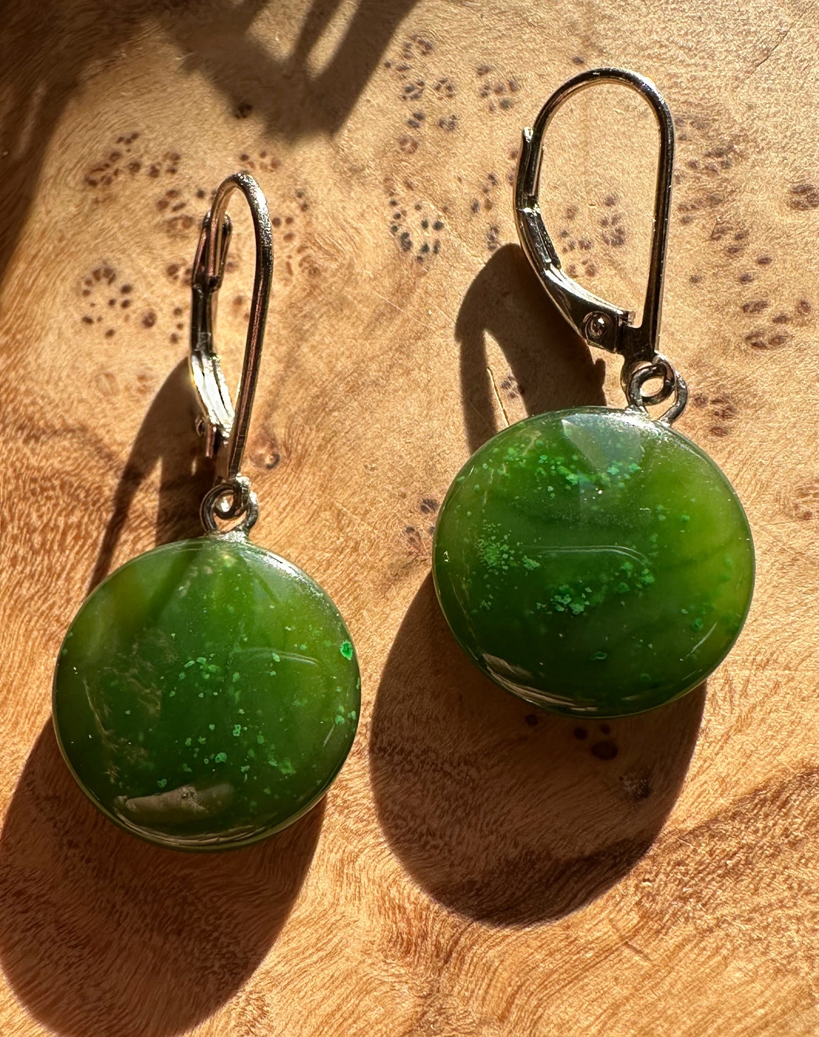 Pair of green round stone earrings with leverback silver hooks on a wooden surface