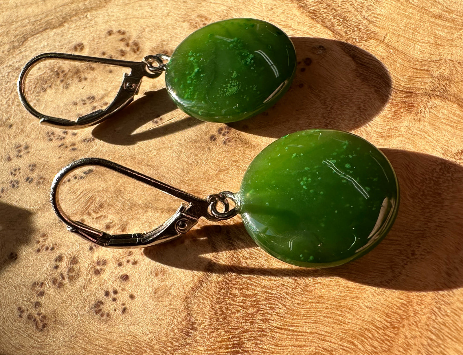 Close up of green jade cabochon earrings with leverback hooks resting on wood