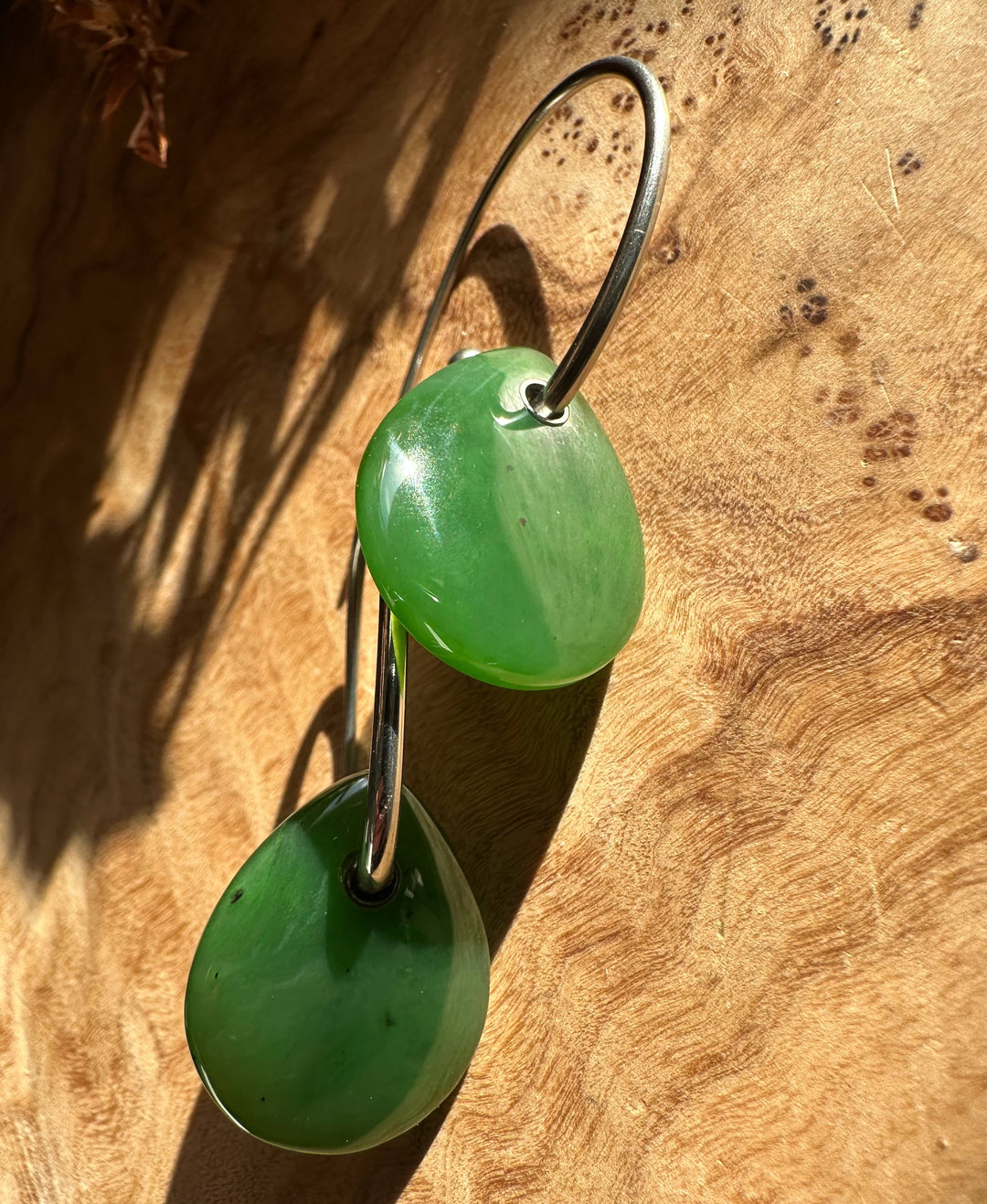 Canadian Jade Earrings with two bright green jade teardrops linked by a curved silver hoop on a wood surface