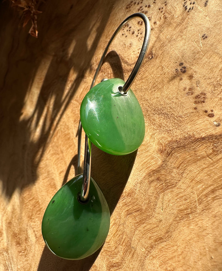 Canadian Jade Earrings with two bright green jade teardrops linked by a curved silver hoop on a wood surface