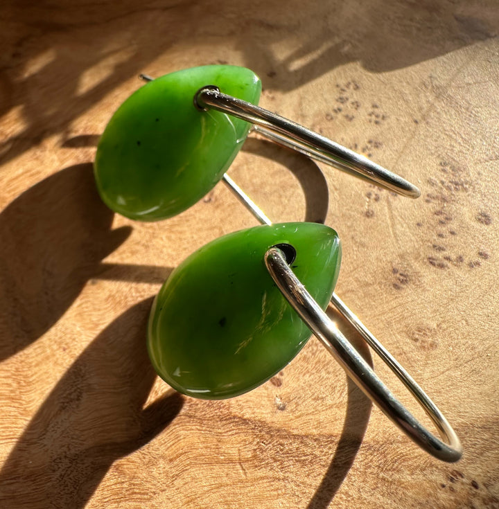 Top-down view of Canadian Jade Earrings two green jade drops on a silver circular hoop against wood grain