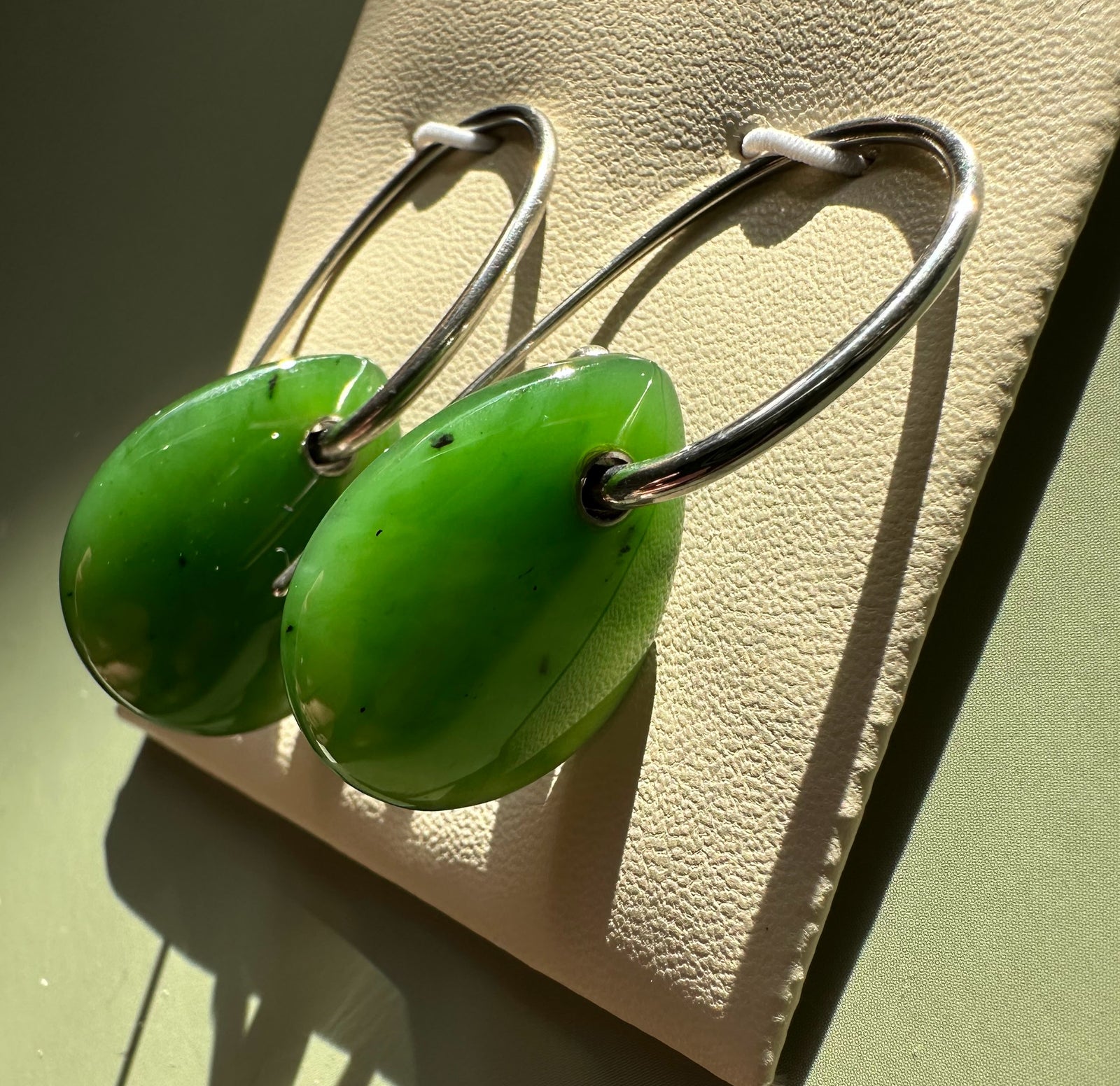 Two lime green circular jade disc earrings on silver hoops displayed on beige background