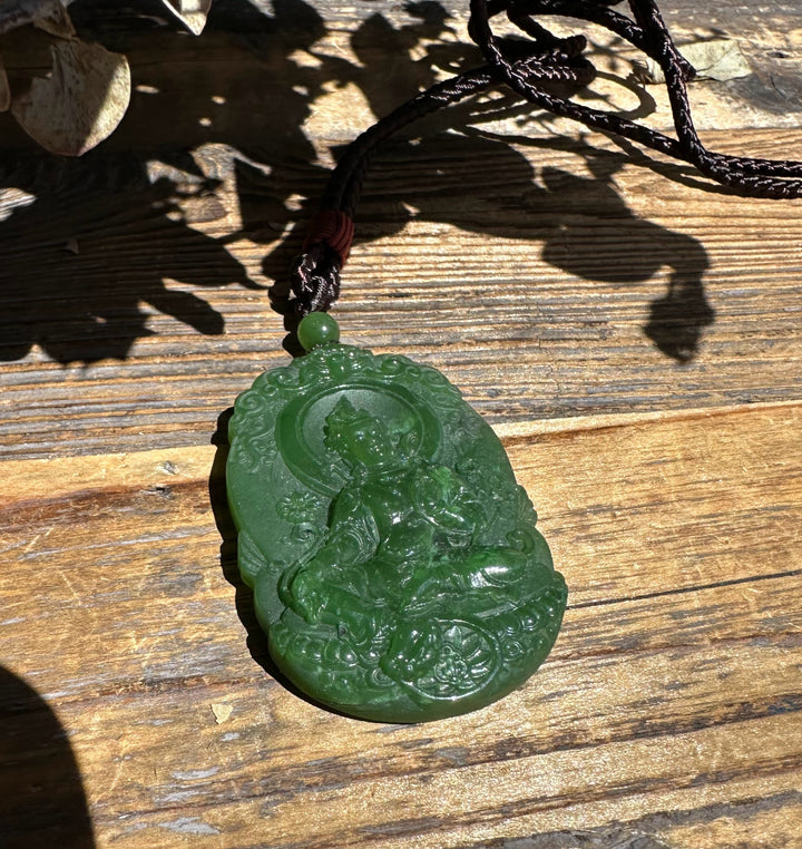 Green jade Guanyin pendant with a seated figure in a circular bezel and ornate surrounding carvings on a braided cord