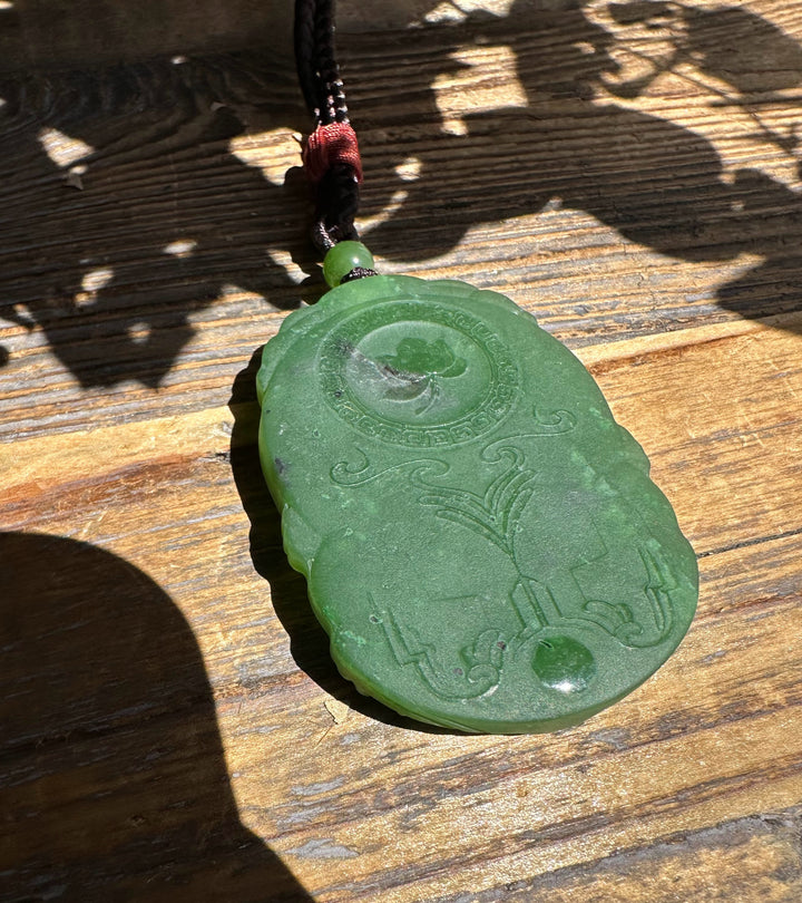 Green jade Guanyin pendant seen from above with circular medallion and decorative engravings along the surface