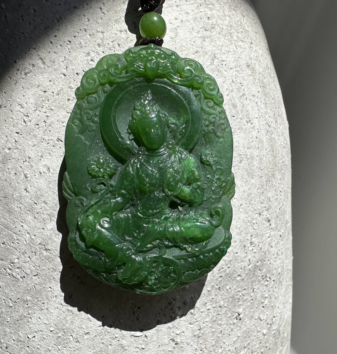 Green jade Guanyin pendant on a textured surface showing a seated deity surrounded by swirling clouds