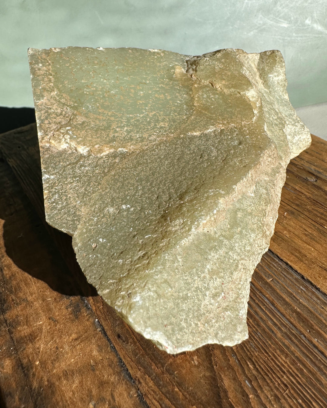 Rough Korean jade rock block with gray green surface on a wooden table.
