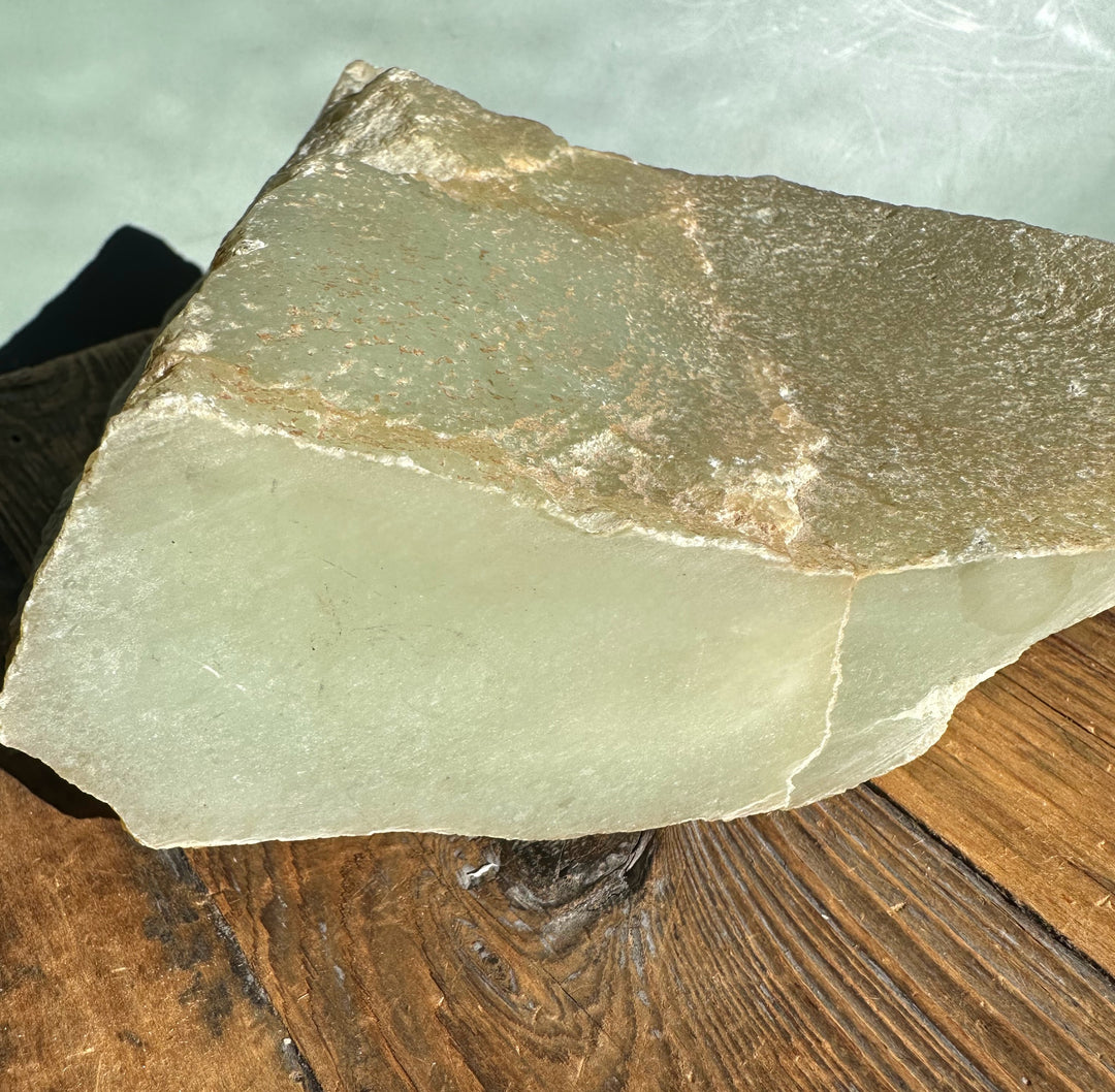 Korean jade rough with pale green face and brown mineral staining along the upper edge.