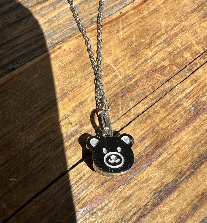 Canadian nephrite jade teddy bear pendant on a silver chain resting on a wooden surface