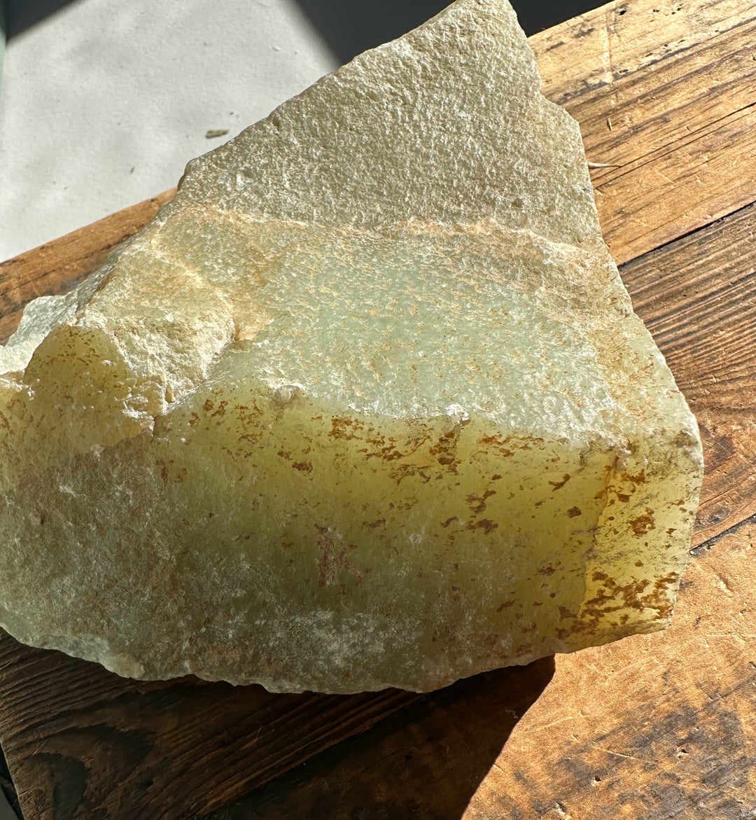 Korean jade rough showing layered gray green surface and brown rust stains on a wooden table.