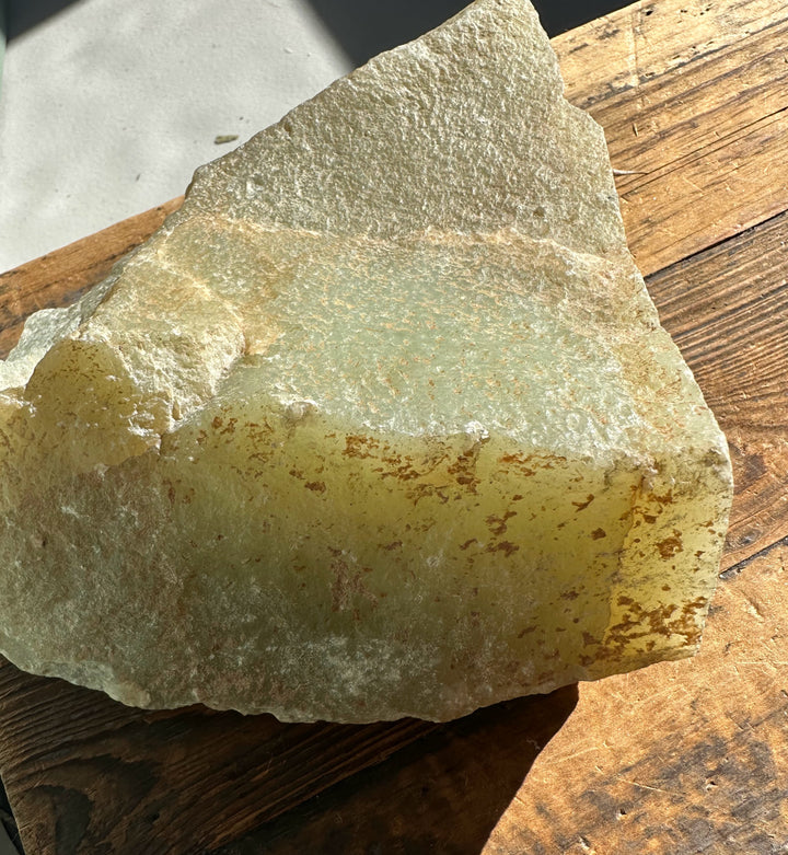 Korean jade rough showing layered gray green surface and brown rust stains on a wooden table.