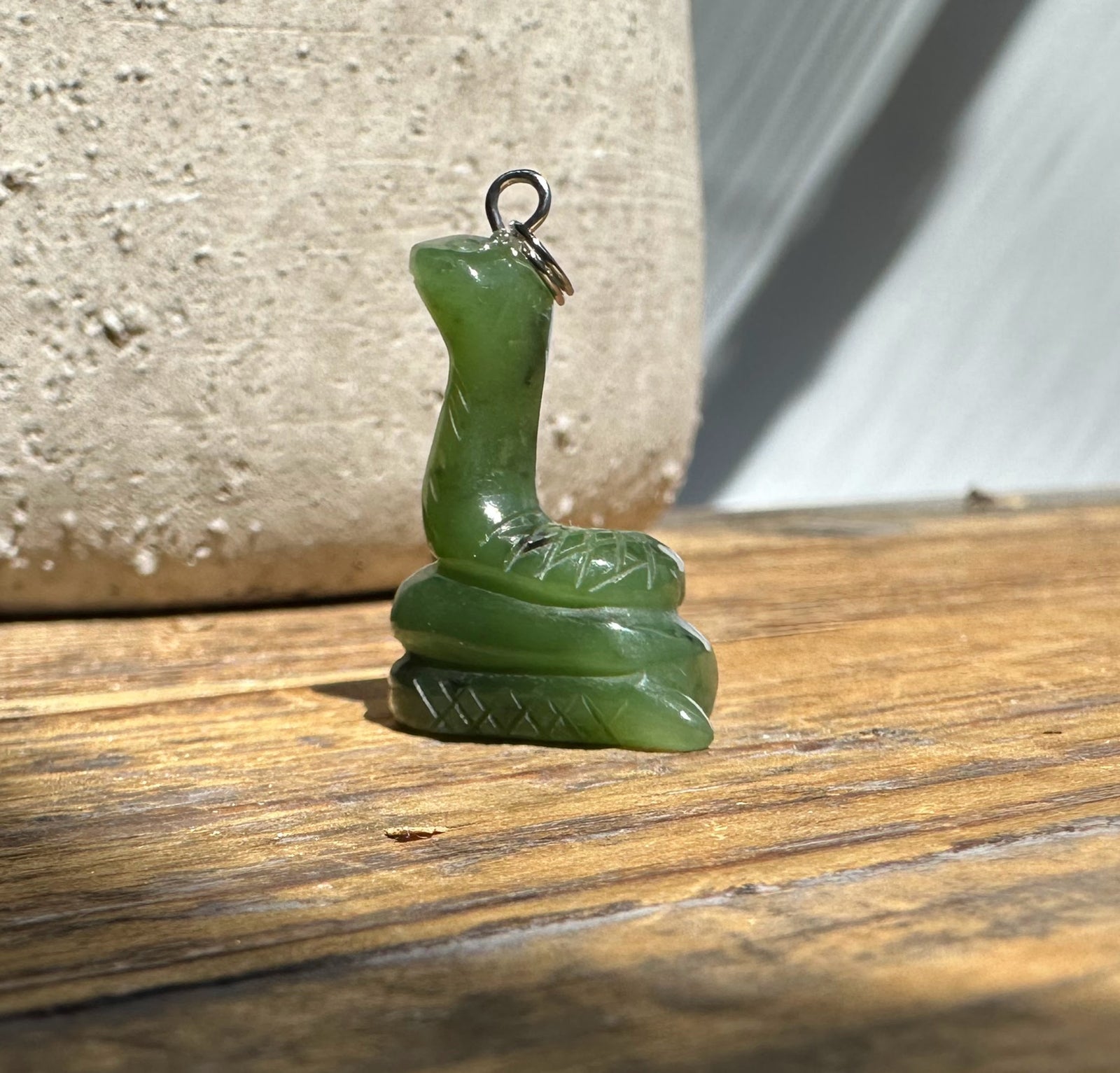 Green jade snake pendant with looped bail standing on a carved base, ready to wear
