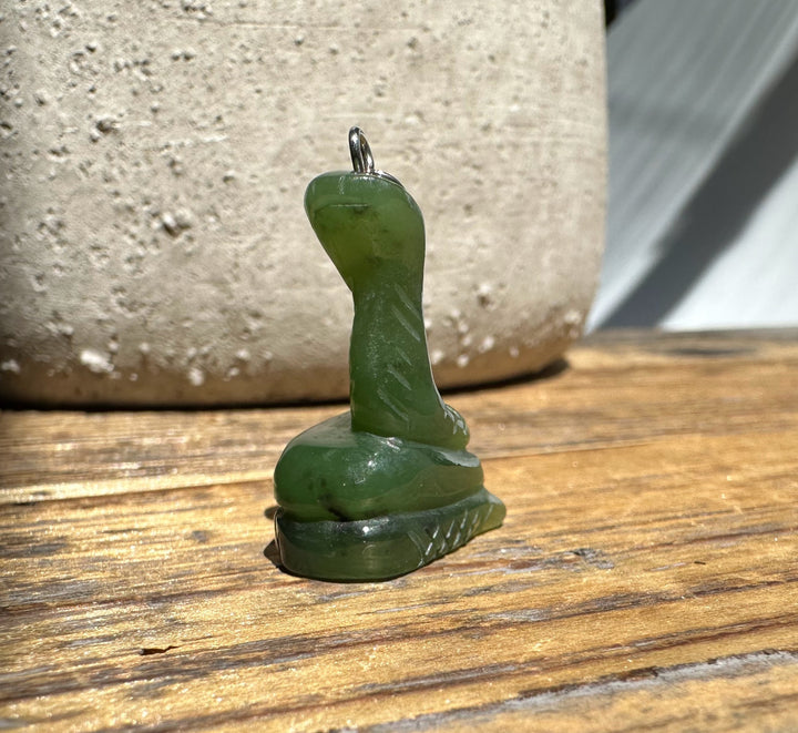 Jade snake pendant perched on a carved base with a metal ring bail against a wooden table