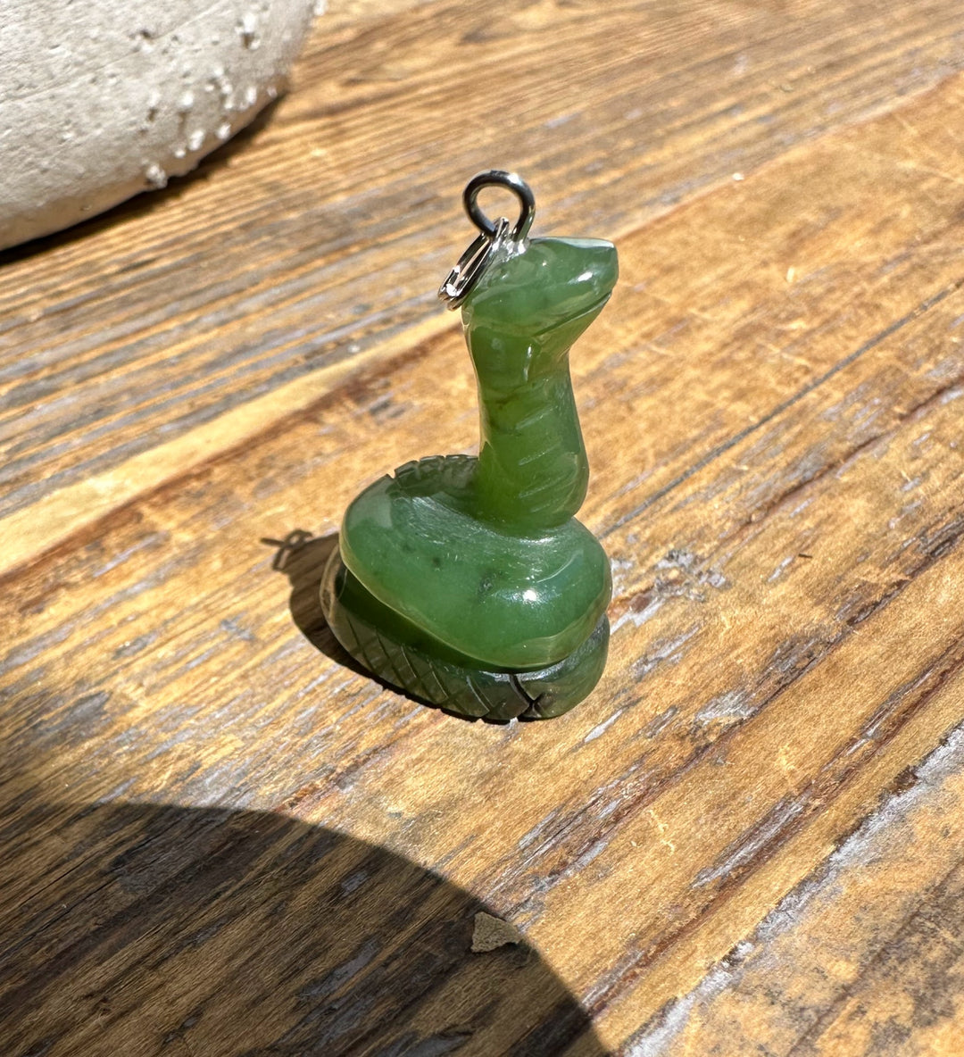 Green 1-inch jade snake pendant with loop bail resting on a wooden surface