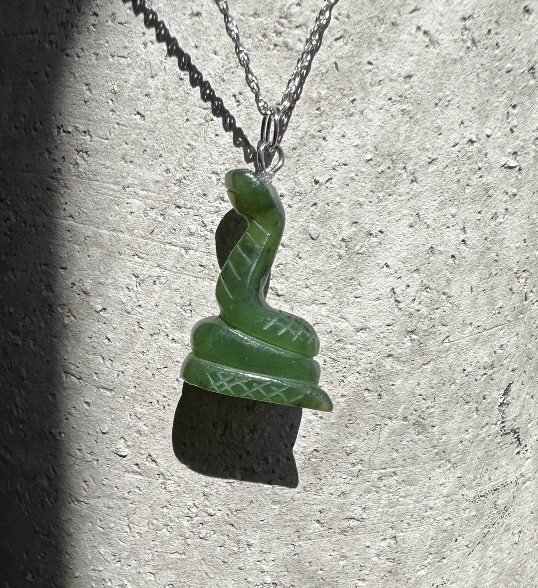 Green 1-inch jade snake pendant on a silver chain against a textured stone background