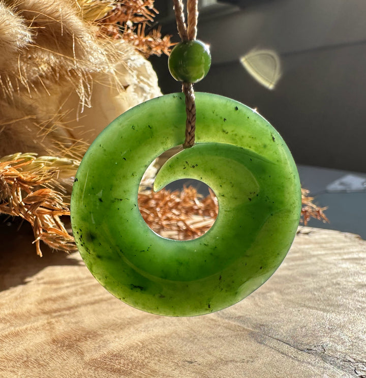 Bright green jade donut pendant with a central hole suspended from a brown cord.