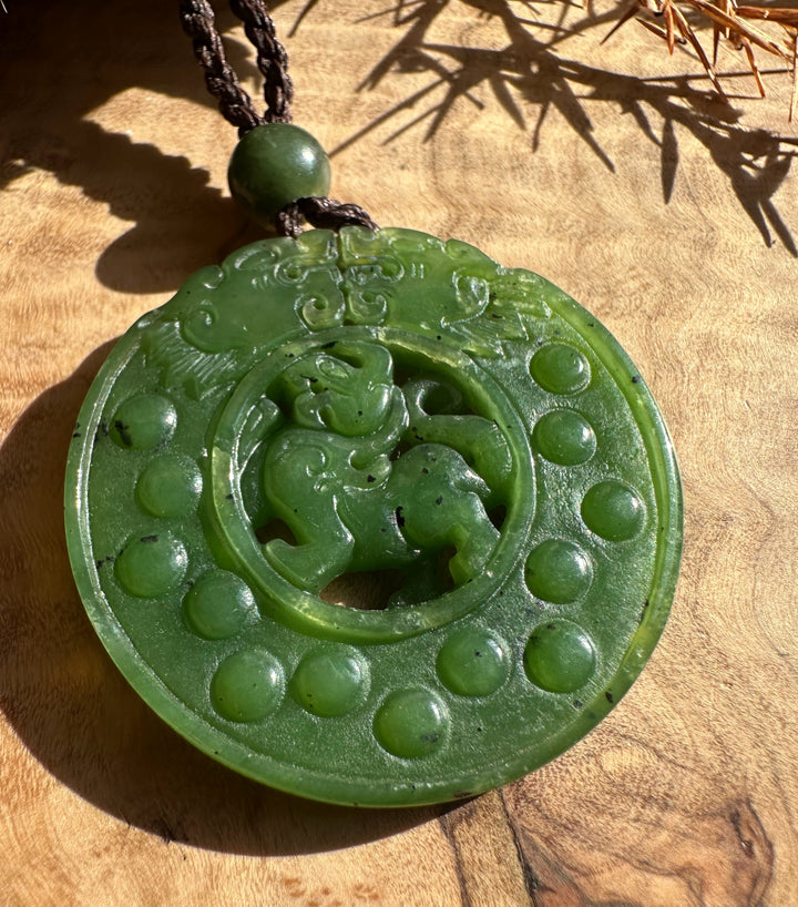 Circular green jade Pixiu pendant with a central carved Pixiu and a dotted outer ring on a dark braided cord.