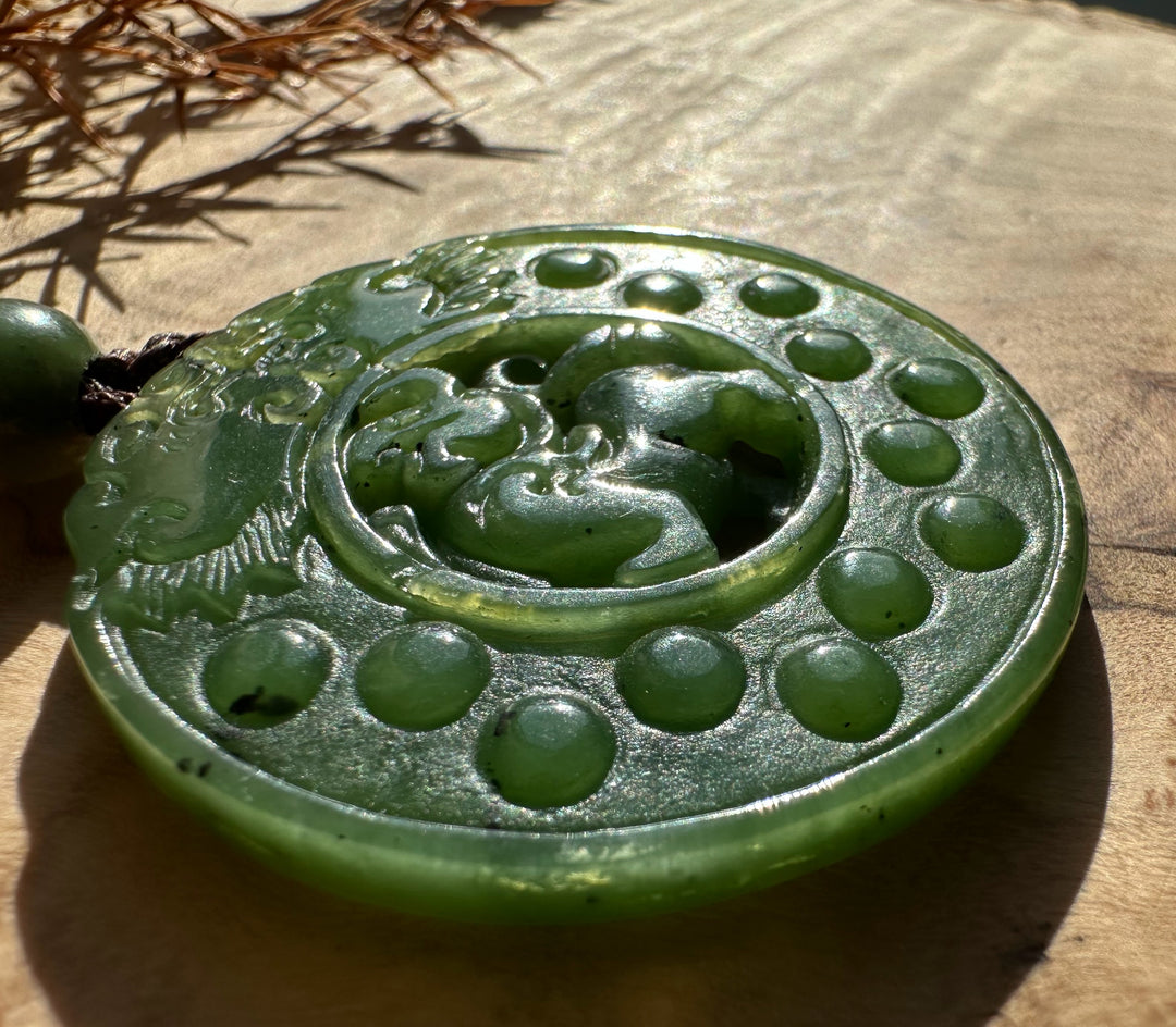 Round green jade Pixiu pendant shown from above with the carved creature and dotted border, hanging on a braided cord with a green bead.
