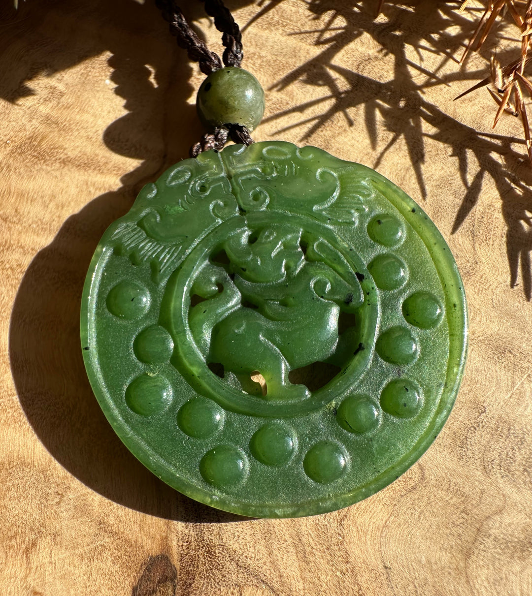 Close-up view of the circular jade Pixiu pendant highlighting the central carving and raised dot border with a dark braided cord.