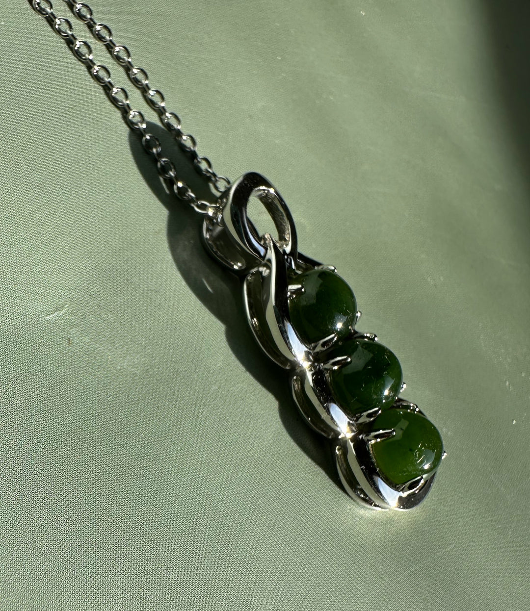 Silver pendant with three round dark green Canadian jade stones set in a curved metal surround on a chain.