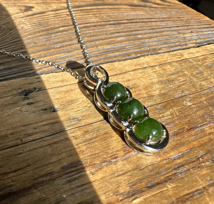 Silver pendant with three green Canadian jade stones on a chain photographed on a wooden surface.