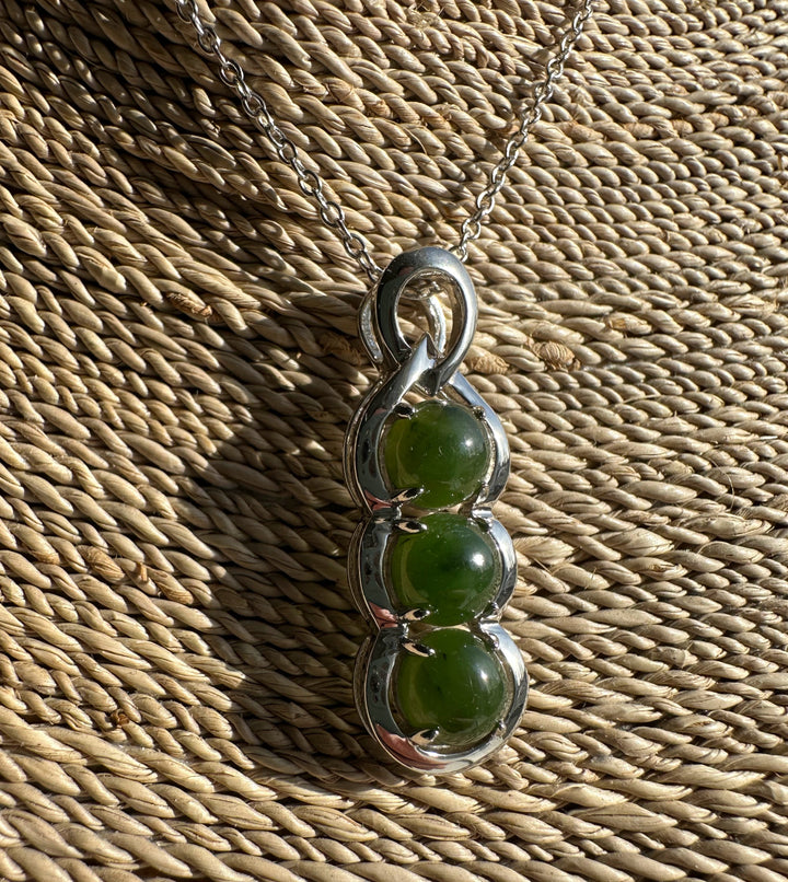 Close up of the pendant showing three stacked green Canadian jade stones in a silver sculpted frame on a woven mat.