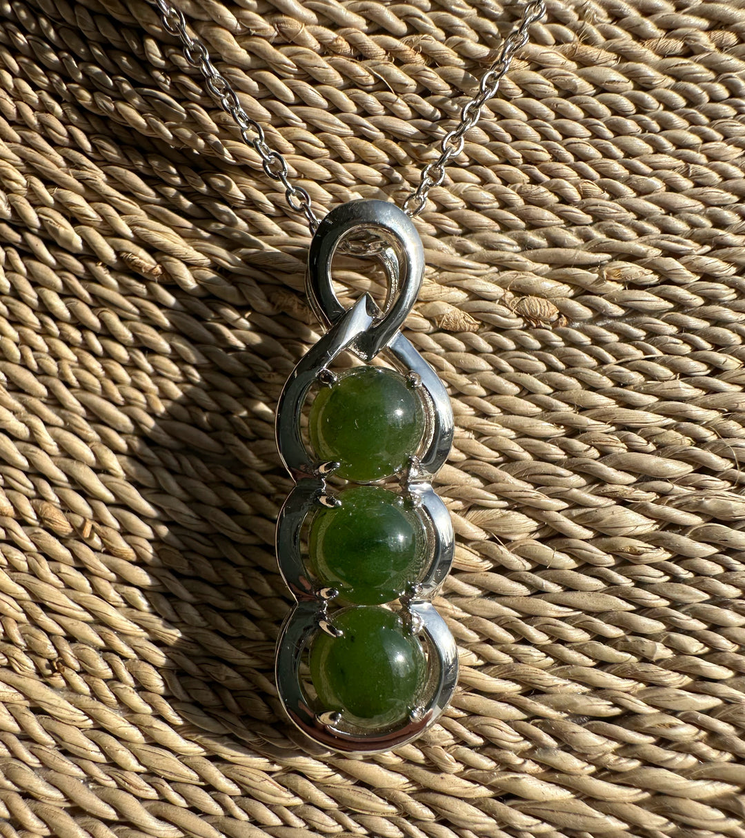 Silver pendant with three green Canadian jade beads set in a looping frame on a chain.