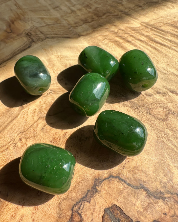 Canadian jade beads vibrant green with holes drilled through shown on a wood surface