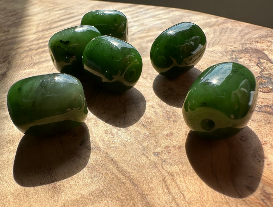 Group of glossy green jade beads with 2 mm holes arranged on a wooden surface.