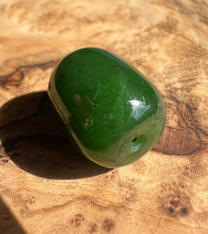 Glossy green jade bead with a rounded surface resting on a brown textured background