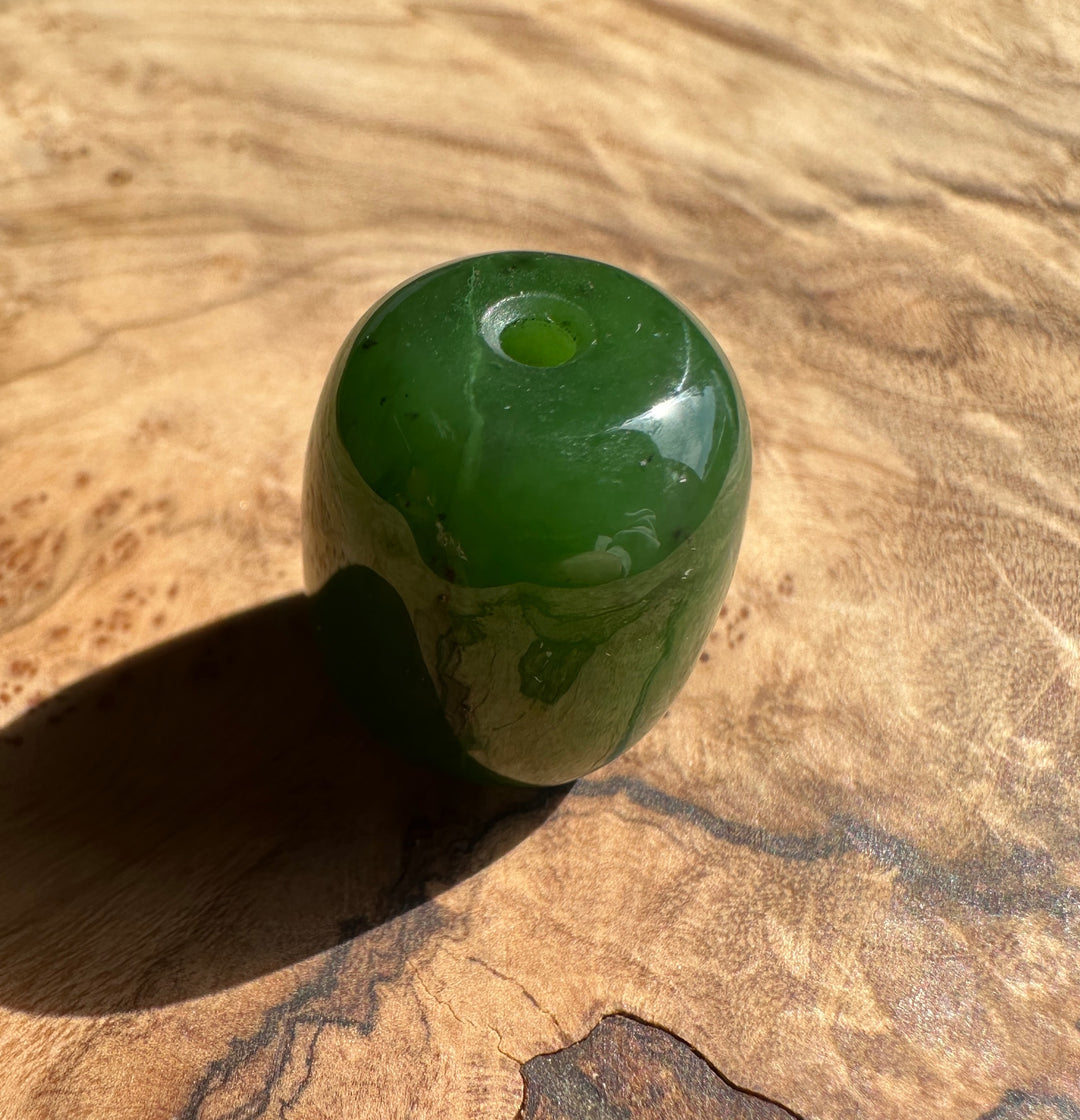 Green Canadian jade bead 15x18 mm with a 2 mm hole resting on a wood surface.
