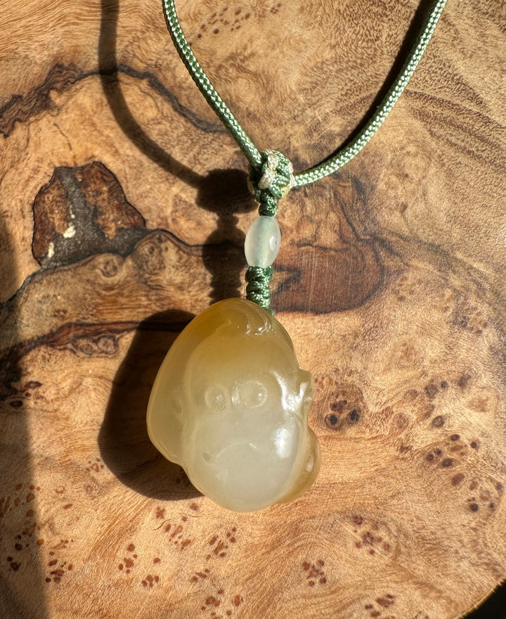 Green braided cord knotted with pale jade bead and a pale honey jade pendant against a wooden surface