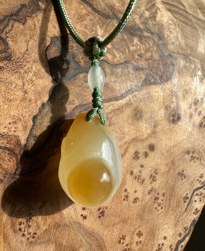 Close-up of green knotted cord with pale jade bead above a yellow honey jade pendant on a wood background