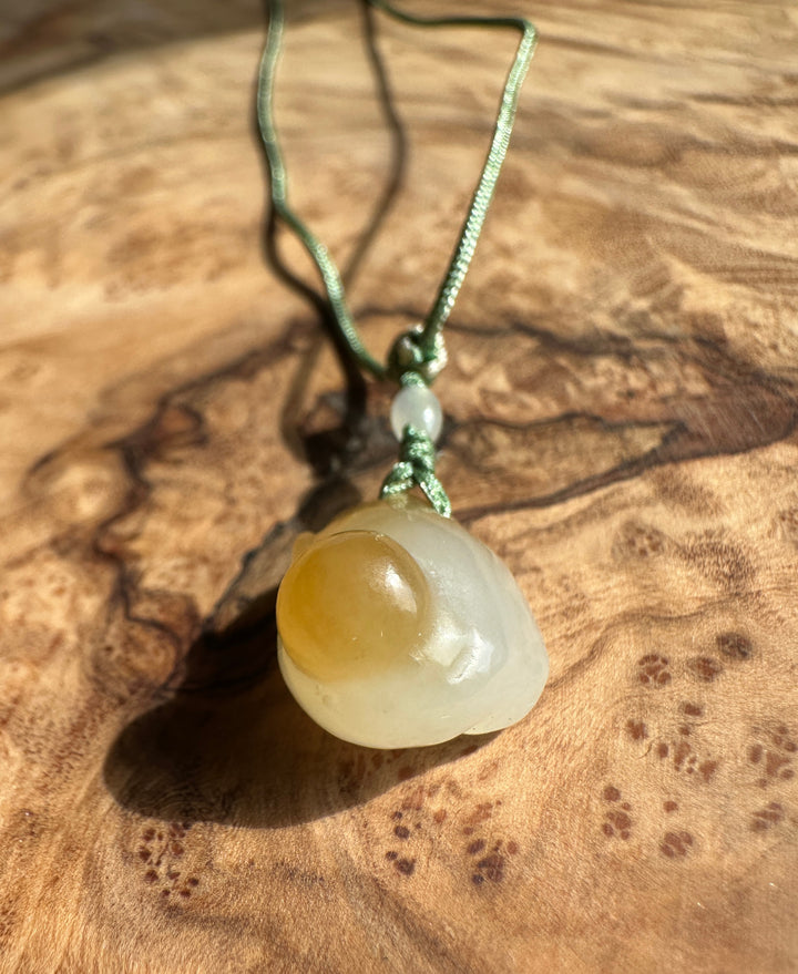 Small honey white nephrite jade monkey pendant on a green braided cord resting on a wood surface