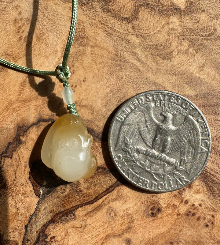 Close up of green cord knot with a pale jade bead and the honey white pendant below on a wood background