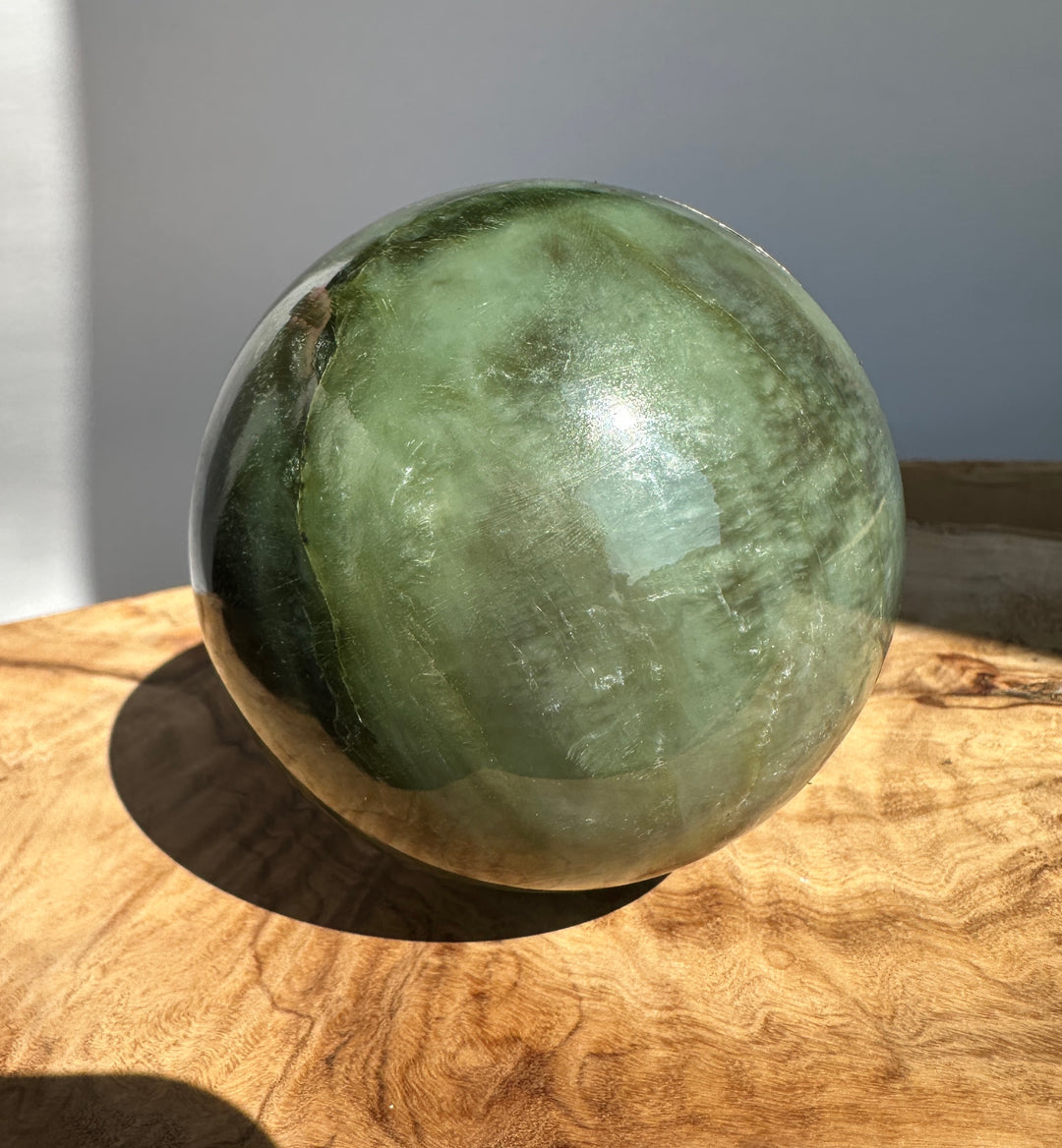 Green Canadian Jade 80mm sphere resting on a wooden surface with natural cracks