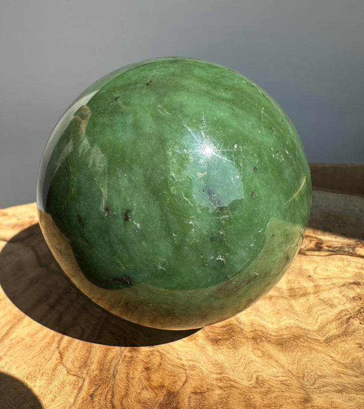 Canadian Jade 80mm sphere with glossy green surface and a white dish edge visible