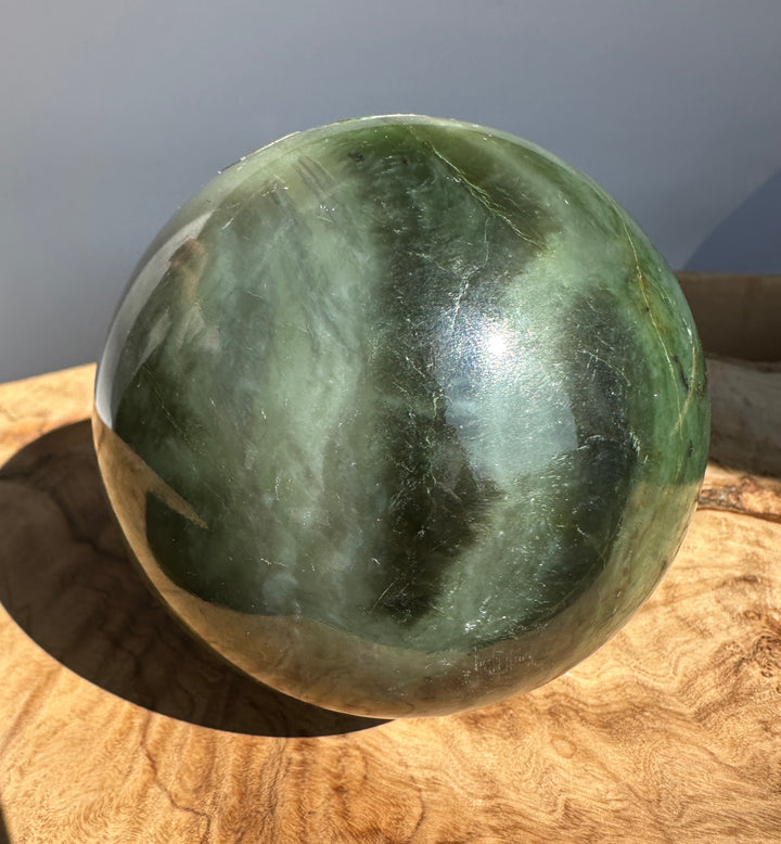 Green Canadian Jade 80mm sphere with vein lines and surface imperfections resting on a wooden surface