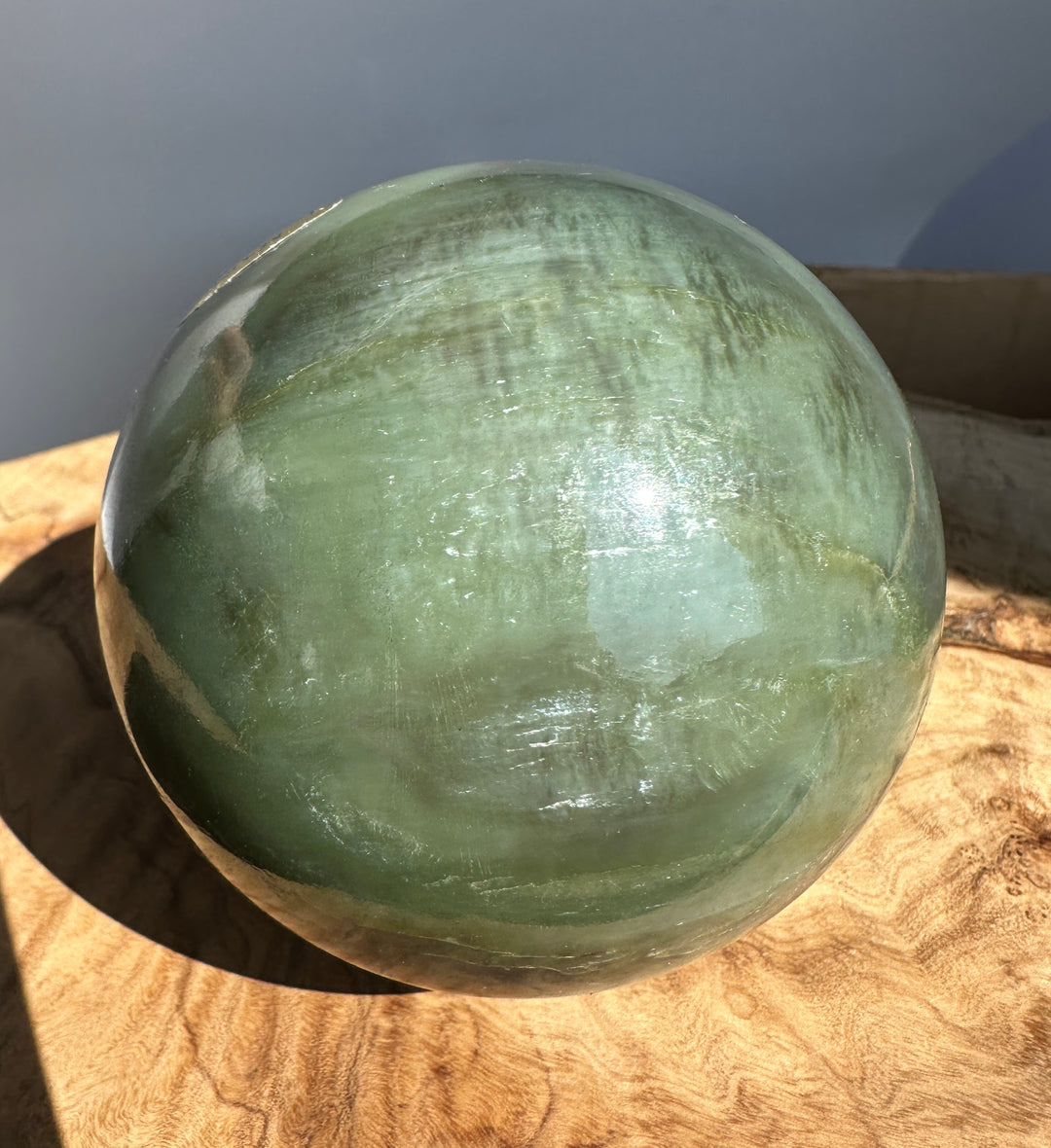 Top portion of a green Canadian Jade 80mm sphere against a pale blue gray backdrop