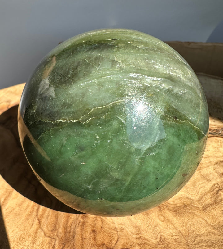 Hands hold a green Canadian Jade 80mm sphere with visible cracks and polished surface