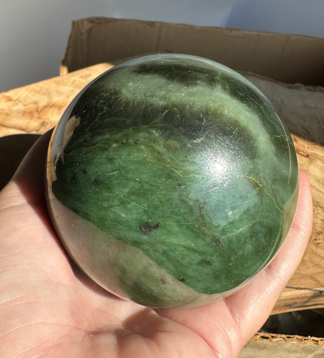 Person cupping a green Canadian Jade 80mm sphere showing veining and small imperfections