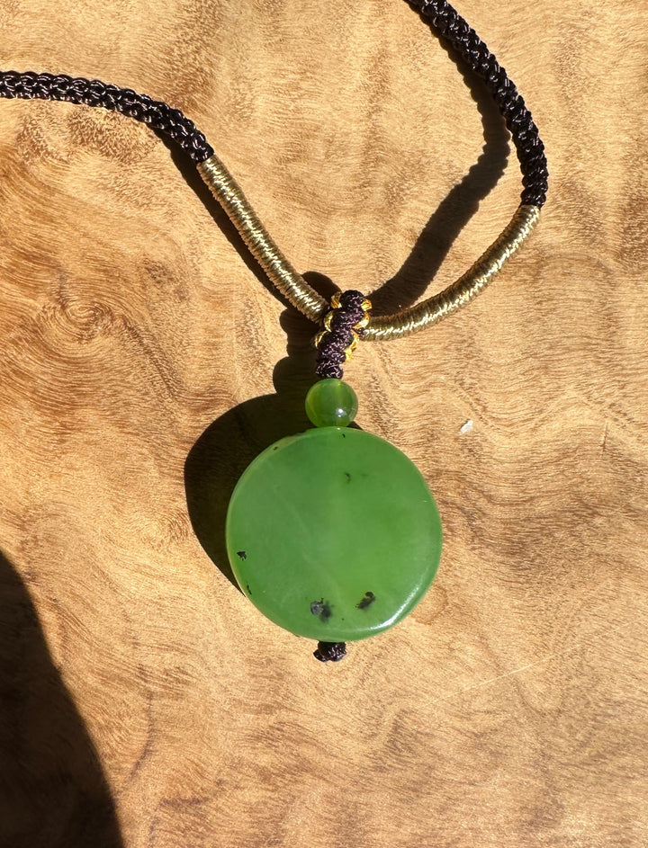 Apple green Siberian jade pendant on black and gold braided cord against a wood background.