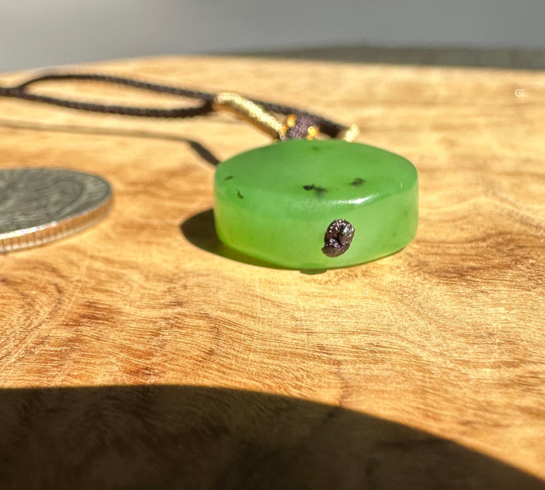 Side view of the apple green jade pendant with gold wrapped cord and purple knot detail on wood.