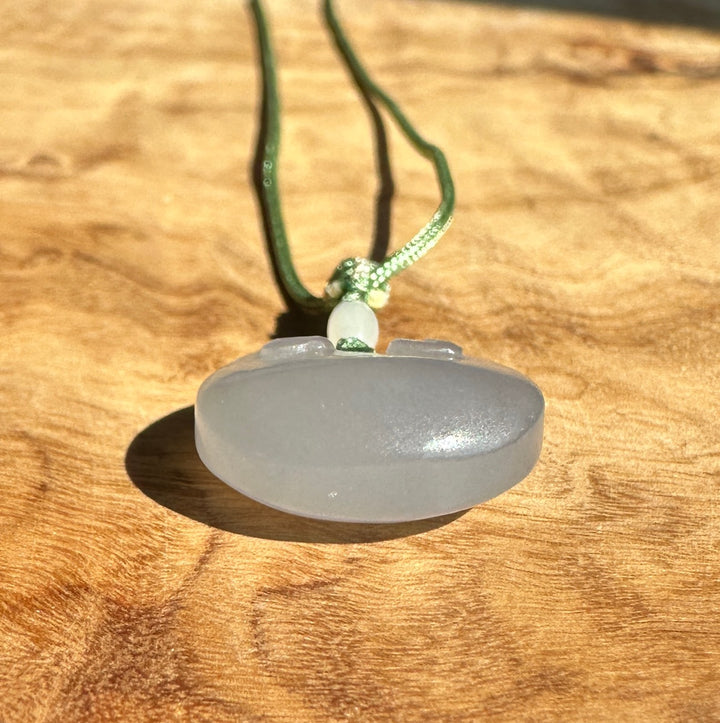 Knot tied in green nephrite cord with a small white bead and a pale jade pendant beneath on a wood background