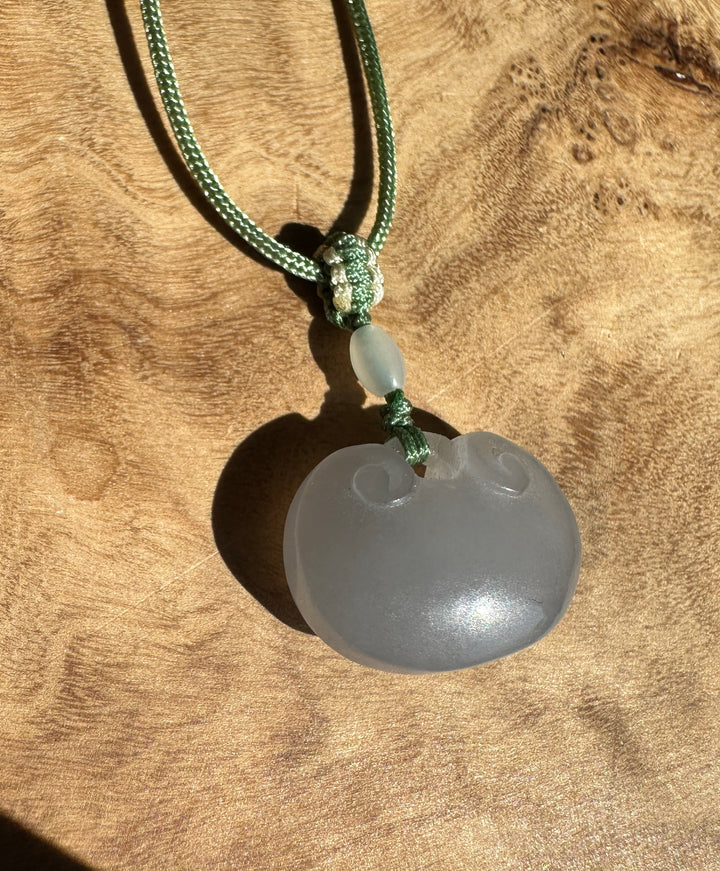 Dainty pale gray nephrite jade Ruyi pendant on a green braided cord with a knot against a wood surface