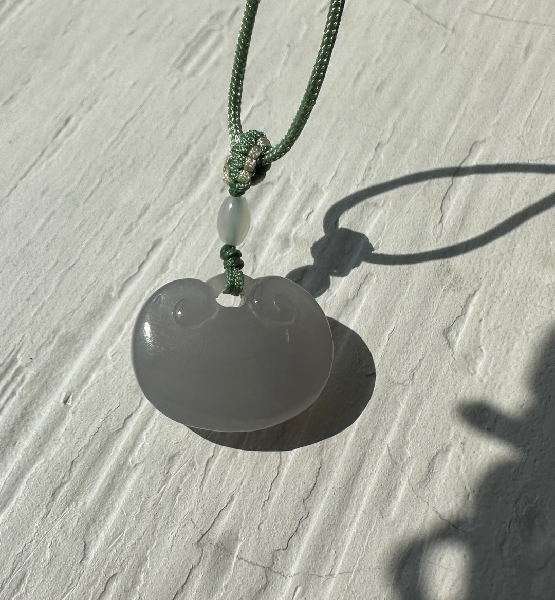 Close up of a green braided cord knot holding a pale jade bead pendant.