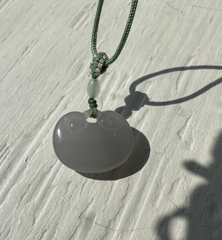 Close up of a green braided cord knot holding a pale jade bead pendant.