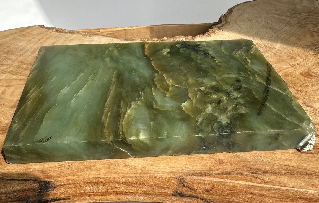 Rough jade slab in green hues with natural veins and jagged edges on a white surface